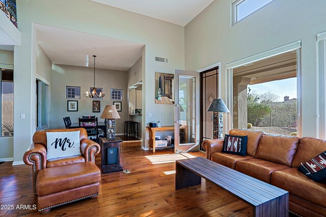 living area with visible vents, baseboards, hardwood / wood-style floors, a high ceiling, and a notable chandelier