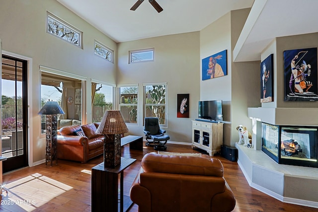 living room with baseboards, a multi sided fireplace, a high ceiling, and wood finished floors