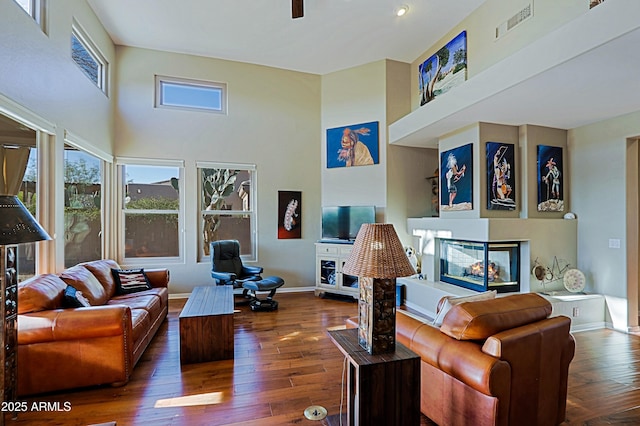 living area with wood-type flooring, baseboards, visible vents, and a multi sided fireplace