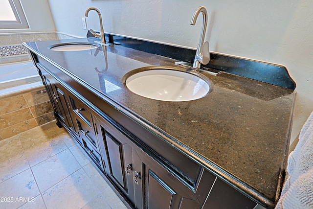 bathroom featuring a sink, stone tile flooring, double vanity, and a textured wall