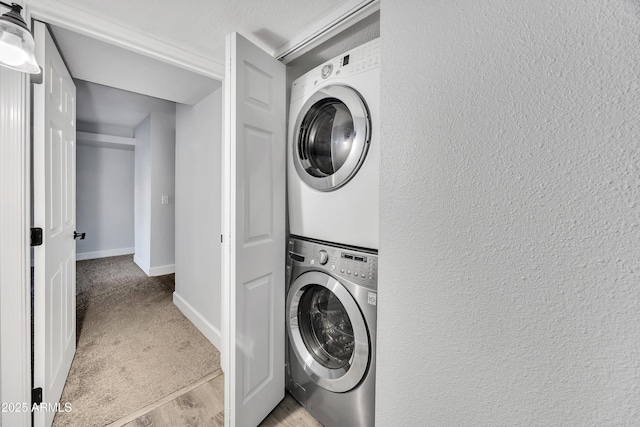 washroom with a textured wall, stacked washer / dryer, light wood-type flooring, laundry area, and baseboards