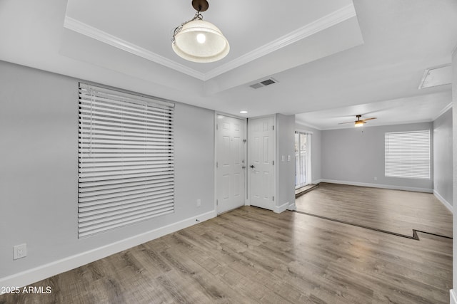 spare room with a tray ceiling, visible vents, crown molding, and light wood finished floors