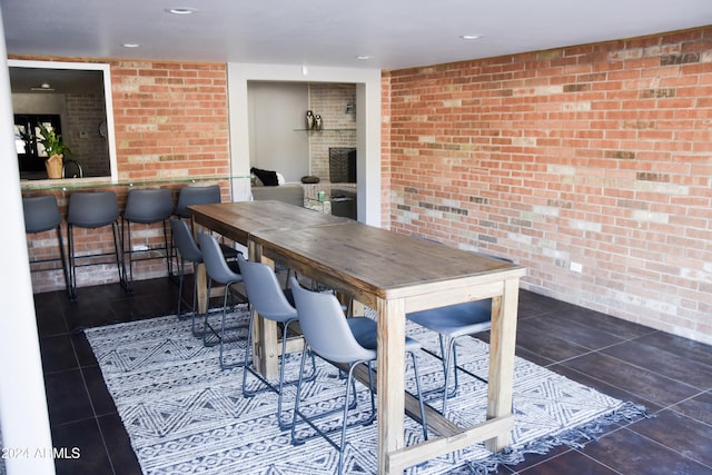 dining area featuring a fireplace, brick wall, and dark tile patterned flooring