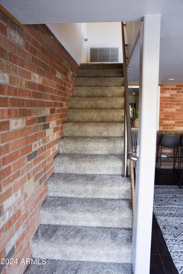 stairs featuring tile patterned flooring and brick wall