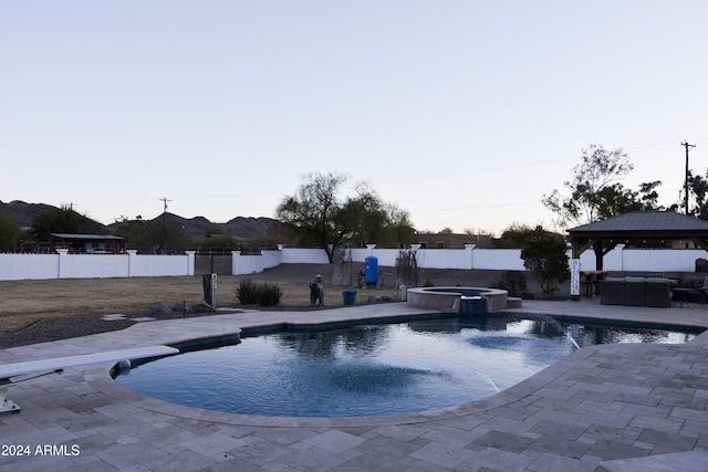 pool at dusk with a gazebo, a patio area, and an in ground hot tub