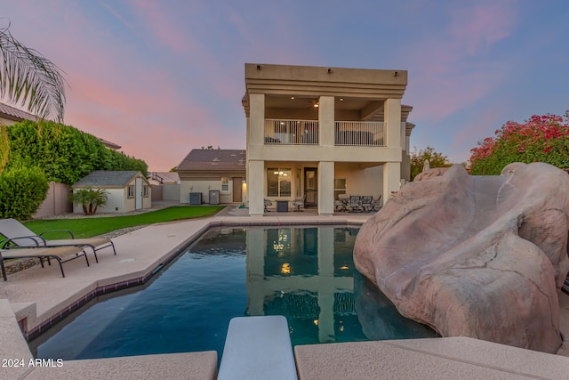 pool at dusk featuring a diving board, a storage unit, a yard, and a patio area