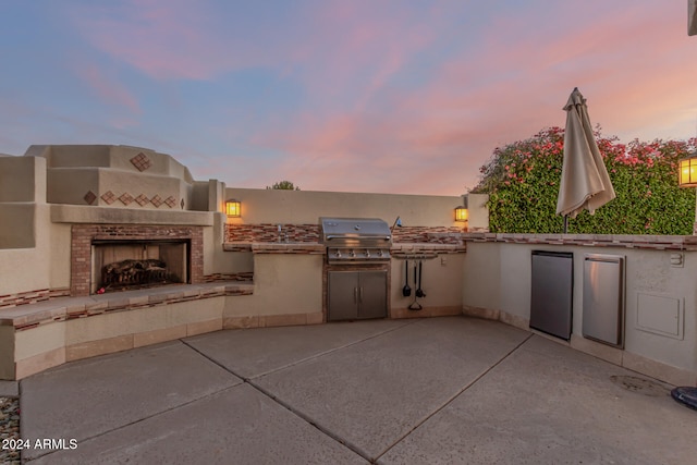 patio terrace at dusk featuring an outdoor kitchen, a grill, and a tile fireplace