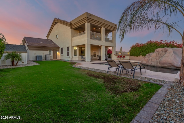 back house at dusk featuring a lawn, central air condition unit, a balcony, and a patio