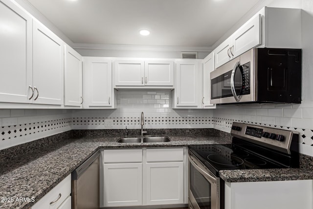 kitchen featuring appliances with stainless steel finishes, a sink, backsplash, white cabinets, and dark stone counters