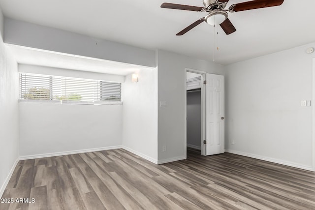 unfurnished bedroom featuring wood finished floors, a spacious closet, and baseboards