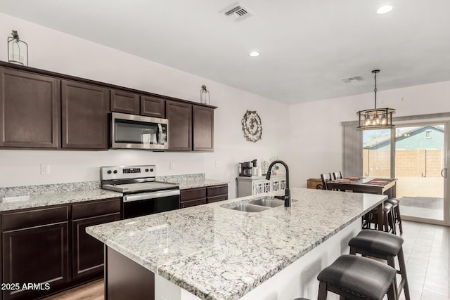 kitchen with dark brown cabinetry, light stone counters, appliances with stainless steel finishes, a breakfast bar, and a sink