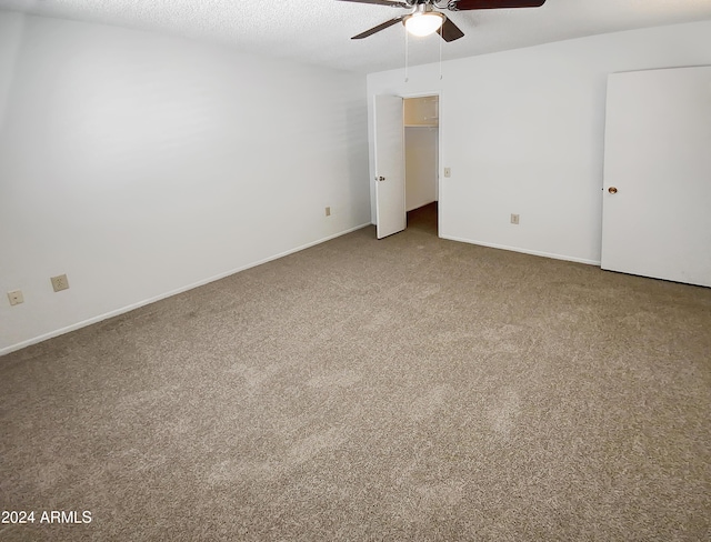 unfurnished bedroom with ceiling fan, a spacious closet, a textured ceiling, a closet, and carpet