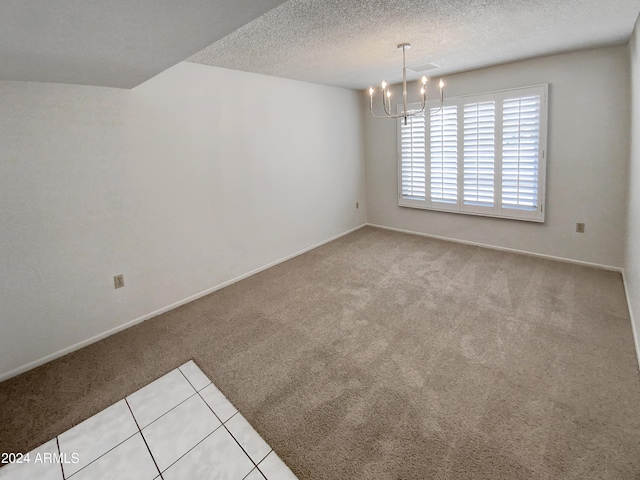 carpeted spare room with a textured ceiling and an inviting chandelier