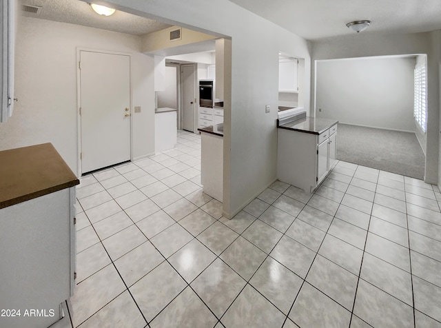 kitchen featuring black oven, light carpet, white cabinets, and a textured ceiling