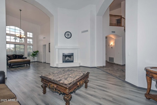 living room featuring a tiled fireplace, hardwood / wood-style floors, a towering ceiling, and a chandelier