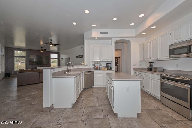 kitchen featuring kitchen peninsula, sink, appliances with stainless steel finishes, a kitchen island, and white cabinetry