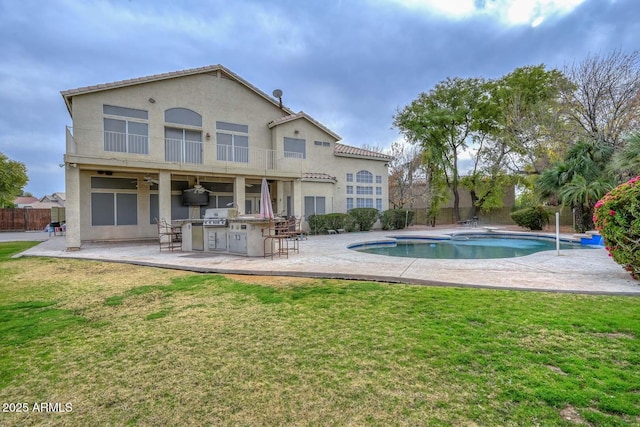 back of property featuring a lawn, a fenced in pool, a balcony, a patio area, and exterior kitchen