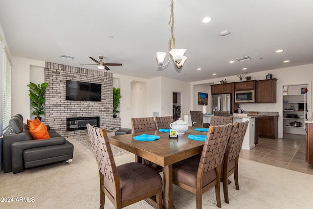 carpeted dining room with a brick fireplace and ceiling fan with notable chandelier