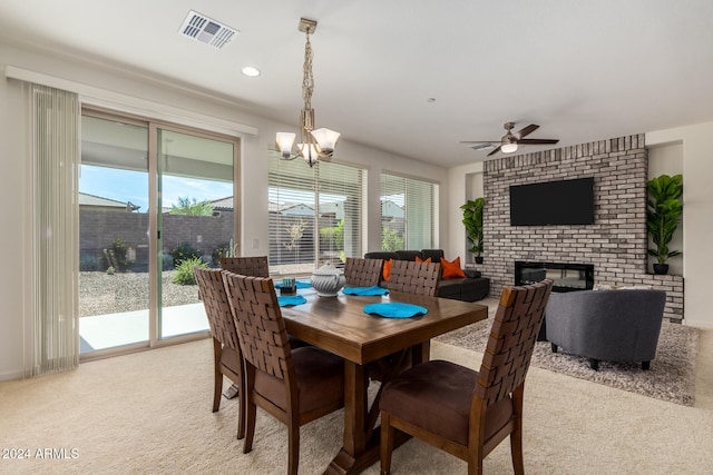 dining area with light colored carpet, a fireplace, and ceiling fan with notable chandelier