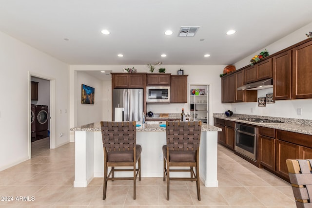 kitchen with appliances with stainless steel finishes, washing machine and clothes dryer, a kitchen breakfast bar, light stone counters, and a center island with sink