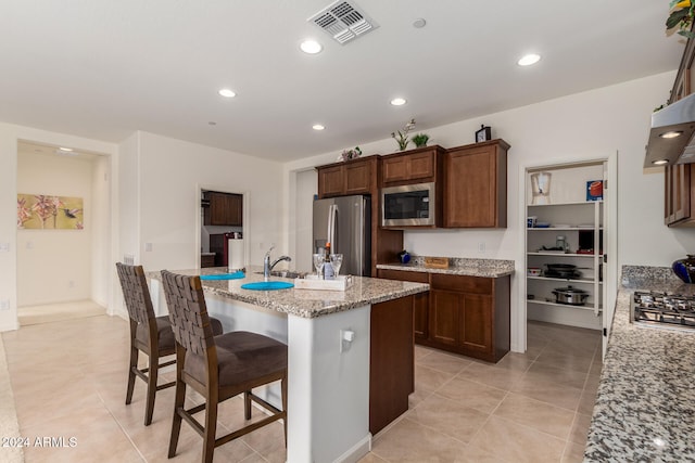 kitchen with light stone counters, a breakfast bar area, light tile patterned floors, an island with sink, and stainless steel appliances