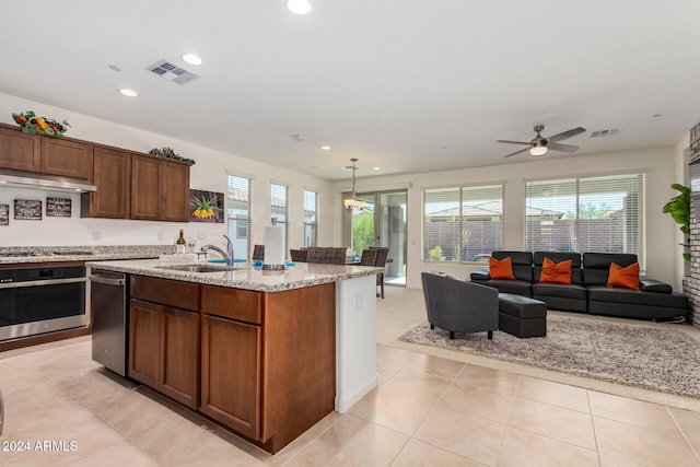 kitchen with light stone countertops, appliances with stainless steel finishes, sink, an island with sink, and light tile patterned floors