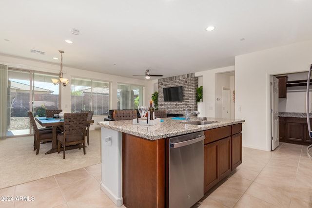 kitchen featuring dishwasher, ceiling fan with notable chandelier, decorative light fixtures, light stone counters, and a kitchen island with sink