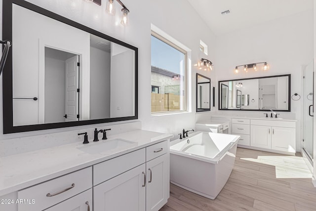 full bath featuring visible vents, a freestanding tub, wood finished floors, and a sink