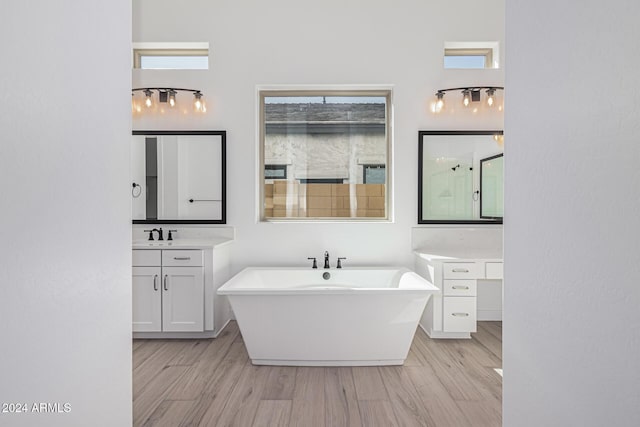 bathroom with a sink, a freestanding tub, two vanities, and wood finished floors