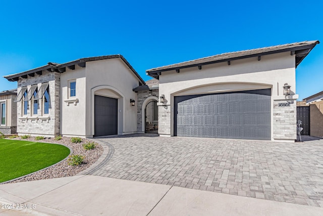 view of front facade with decorative driveway, a tile roof, an attached garage, and stucco siding