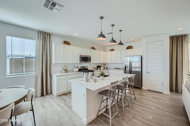 kitchen with a breakfast bar, white cabinetry, hanging light fixtures, appliances with stainless steel finishes, and a kitchen island with sink