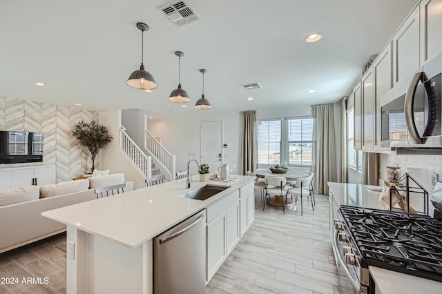 kitchen with sink, white cabinetry, hanging light fixtures, a center island with sink, and stainless steel appliances