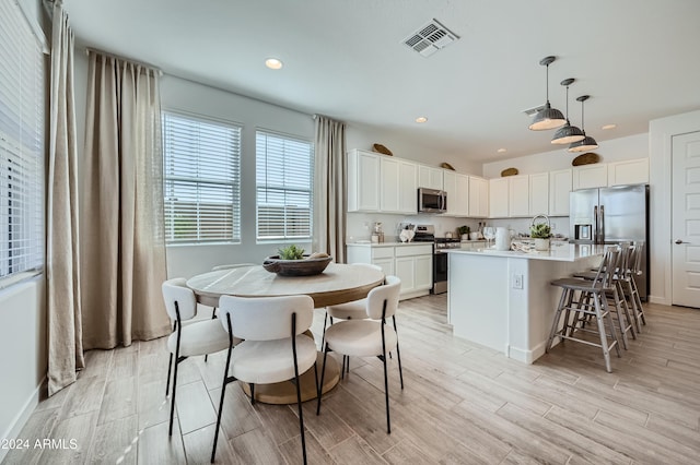 kitchen with appliances with stainless steel finishes, white cabinetry, hanging light fixtures, a center island, and light hardwood / wood-style flooring