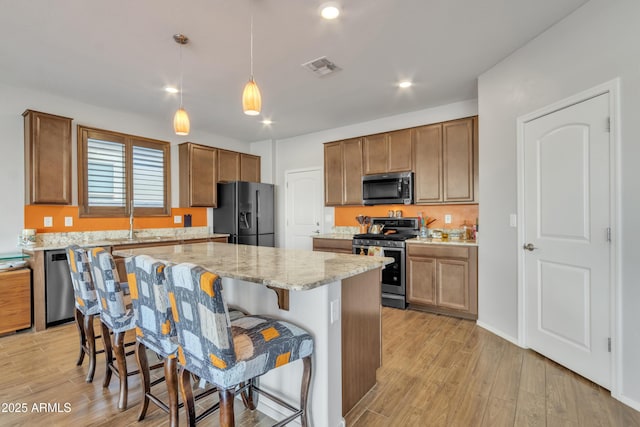 kitchen featuring a center island, a breakfast bar area, visible vents, appliances with stainless steel finishes, and light stone countertops