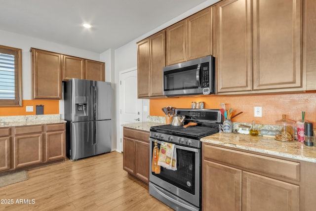 kitchen with brown cabinets, light wood-style flooring, light stone counters, and stainless steel appliances