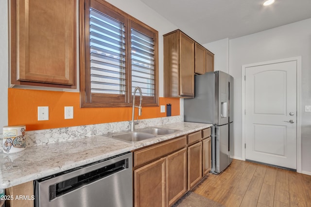 kitchen with appliances with stainless steel finishes, a sink, light wood-style flooring, and brown cabinets