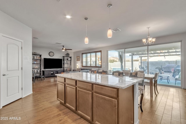 kitchen featuring light stone counters, a kitchen island, visible vents, light wood-style floors, and open floor plan