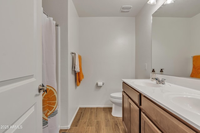 full bathroom with toilet, wood finished floors, a sink, baseboards, and double vanity