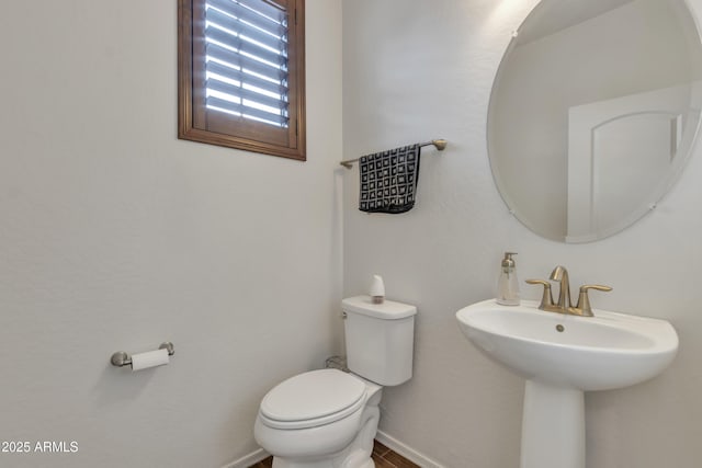 half bath featuring toilet, baseboards, and a sink