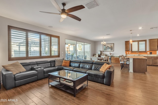 living area with ceiling fan with notable chandelier, a wealth of natural light, visible vents, and wood finished floors