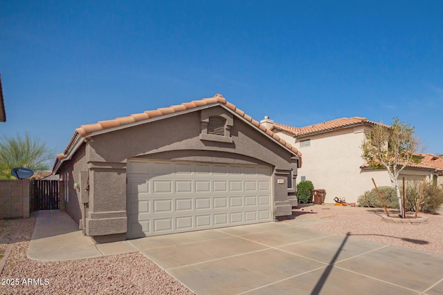 view of property exterior with an attached garage, fence, a tile roof, concrete driveway, and stucco siding