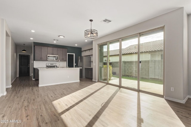 kitchen featuring appliances with stainless steel finishes, light stone counters, a center island, pendant lighting, and dark brown cabinetry