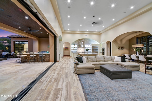 living room with light wood-type flooring, ceiling fan, and a towering ceiling