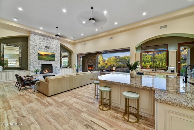 kitchen with cream cabinets, ceiling fan, light hardwood / wood-style flooring, light stone counters, and a stone fireplace