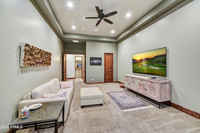 carpeted living room with ceiling fan and a tray ceiling