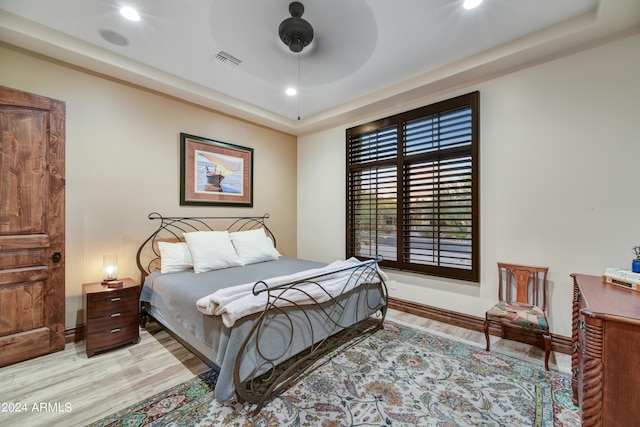 bedroom featuring ceiling fan, light hardwood / wood-style floors, and a raised ceiling