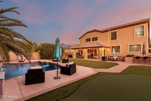 pool at dusk with area for grilling, pool water feature, a patio area, and an outdoor bar