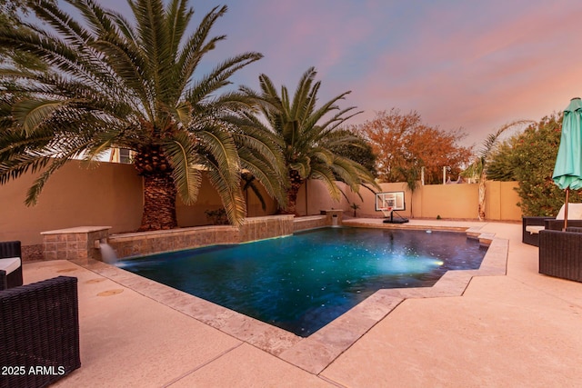 pool at dusk with pool water feature and a patio