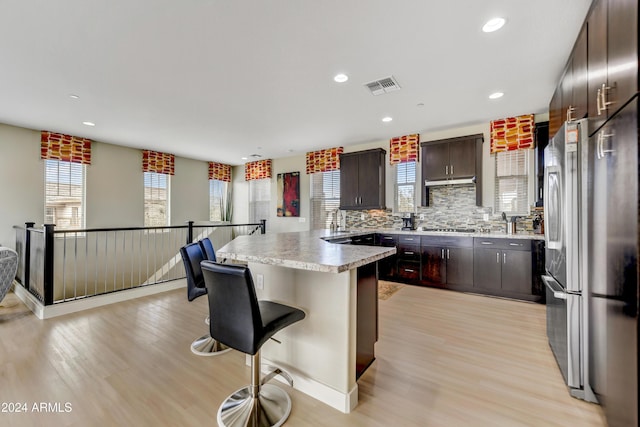 kitchen featuring stainless steel appliances, tasteful backsplash, light wood-type flooring, a breakfast bar area, and dark brown cabinets