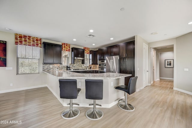 kitchen with kitchen peninsula, decorative backsplash, a breakfast bar area, appliances with stainless steel finishes, and dark brown cabinetry